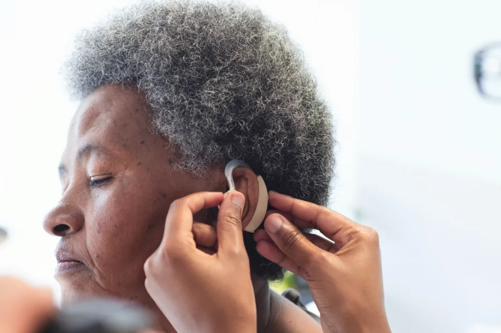 A caregiver helping an older adult place a behind the ear hearing aid